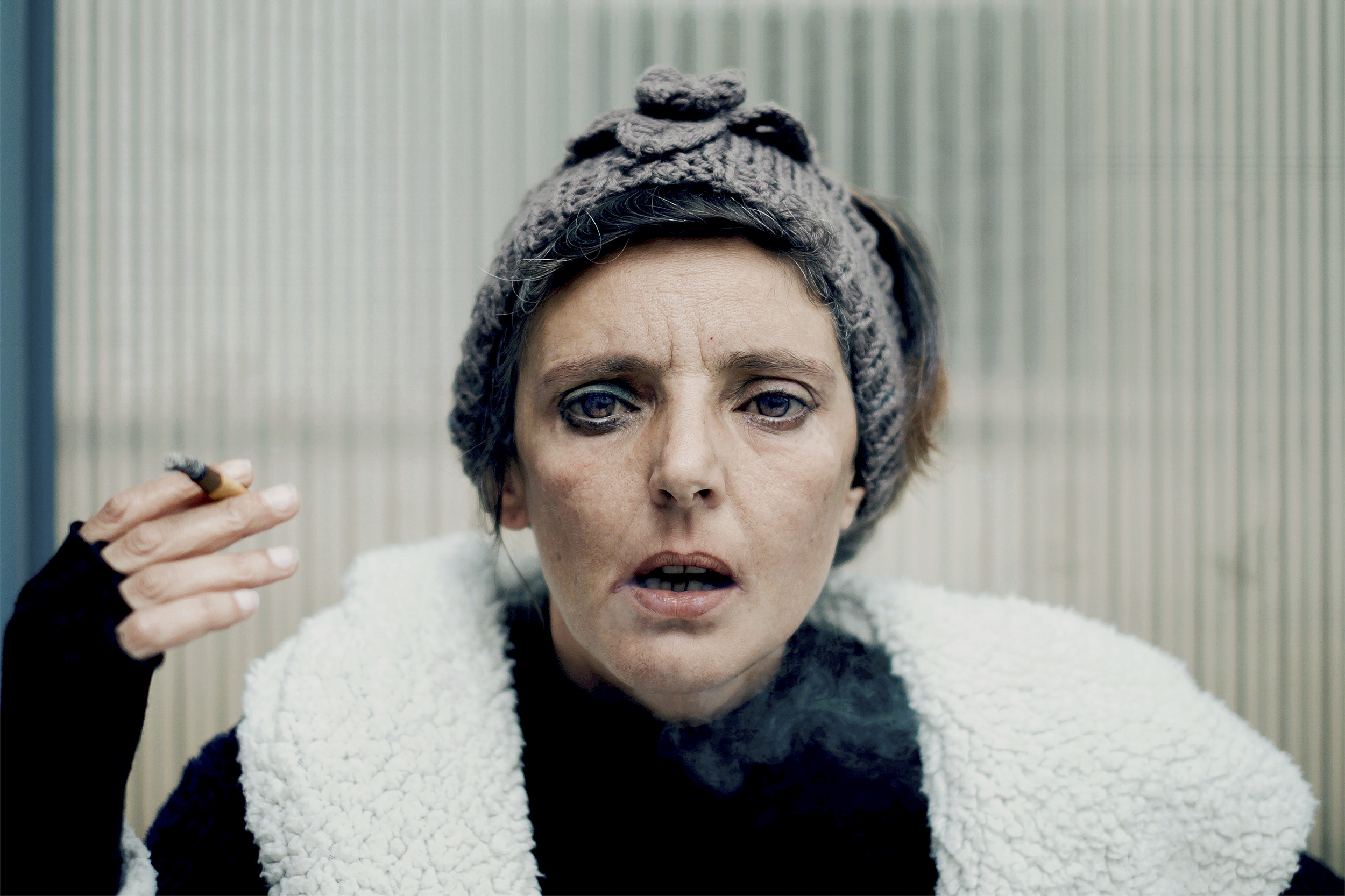 Mulher encara a câmara com olhar expressivo e segura cigarro com a mão direita.