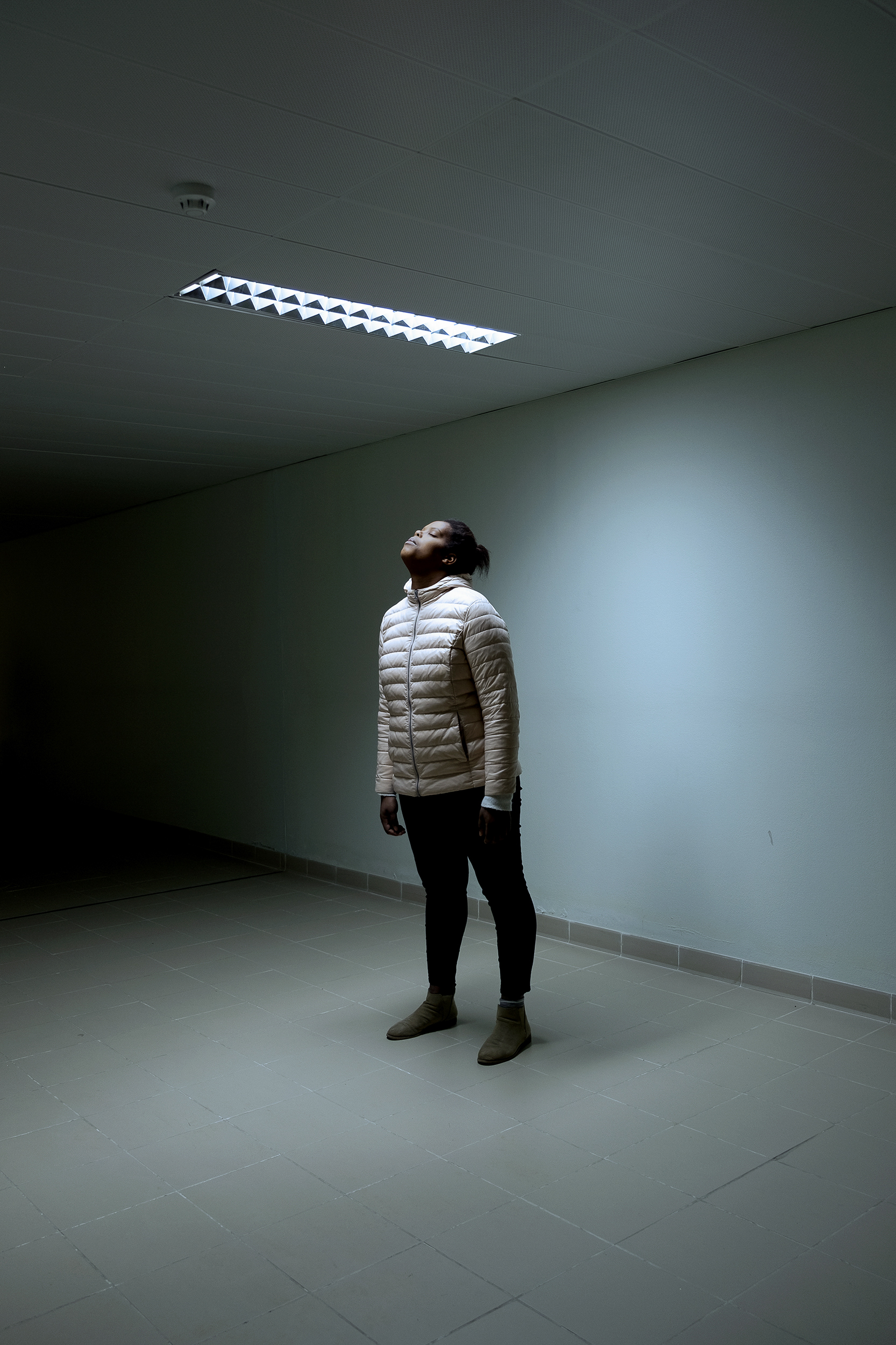 Mulher em pé num corredor azul, cabeça virada para o tecto de olhos fechados.