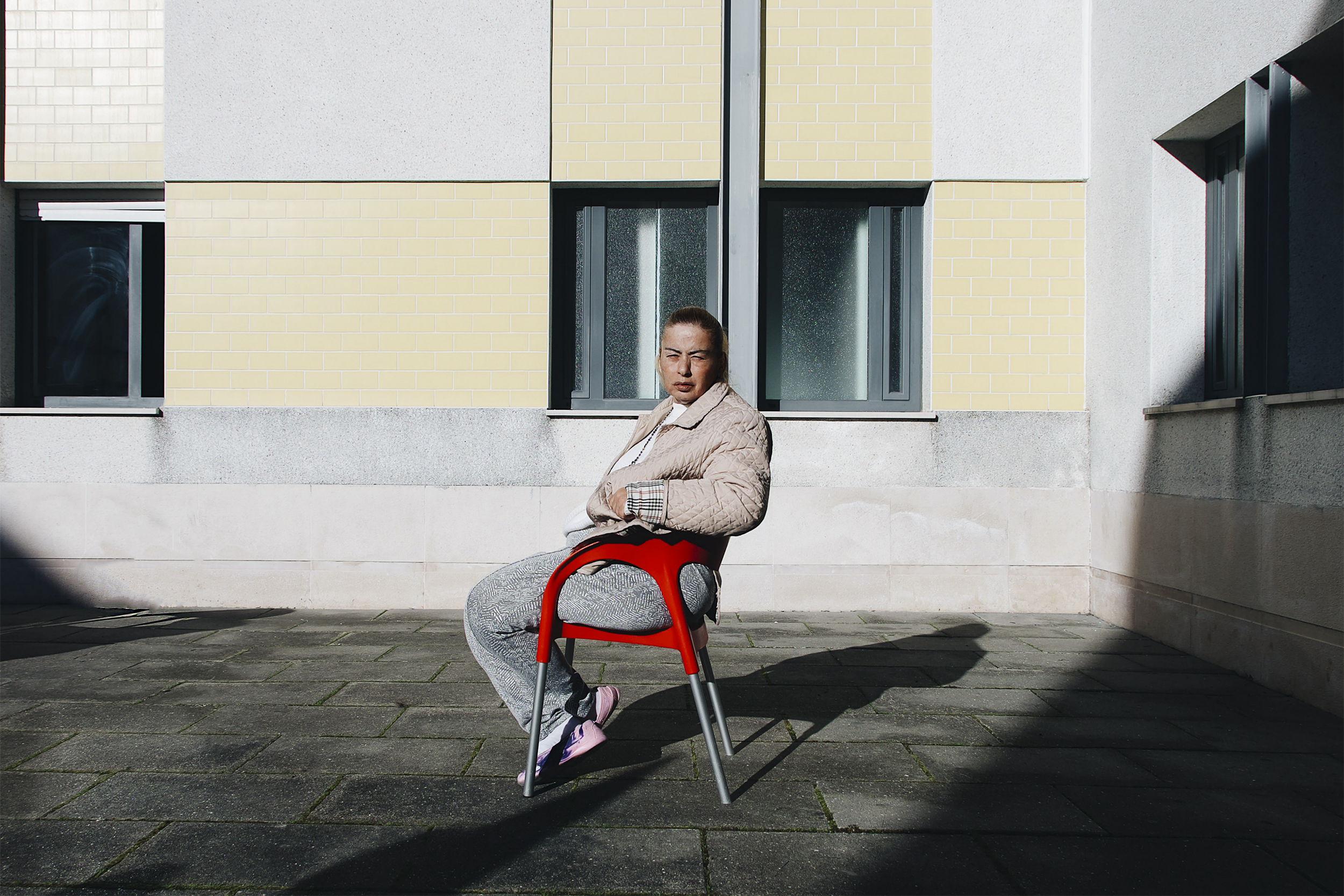 Mulher encara a câmara, sentada em cadeira vermelha entre a sombra e a luz.