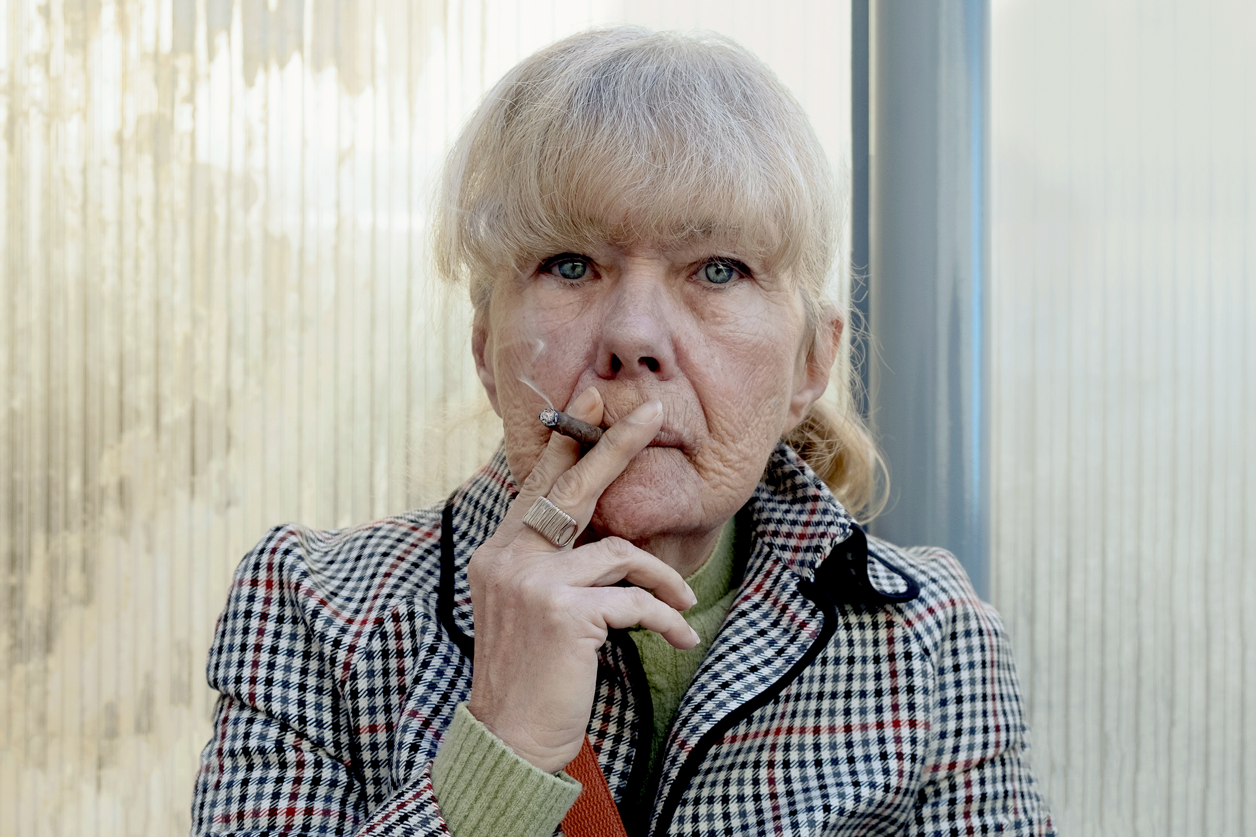 Mulher de olhos azuis encara a câmara enquanto fuma um cigarro.