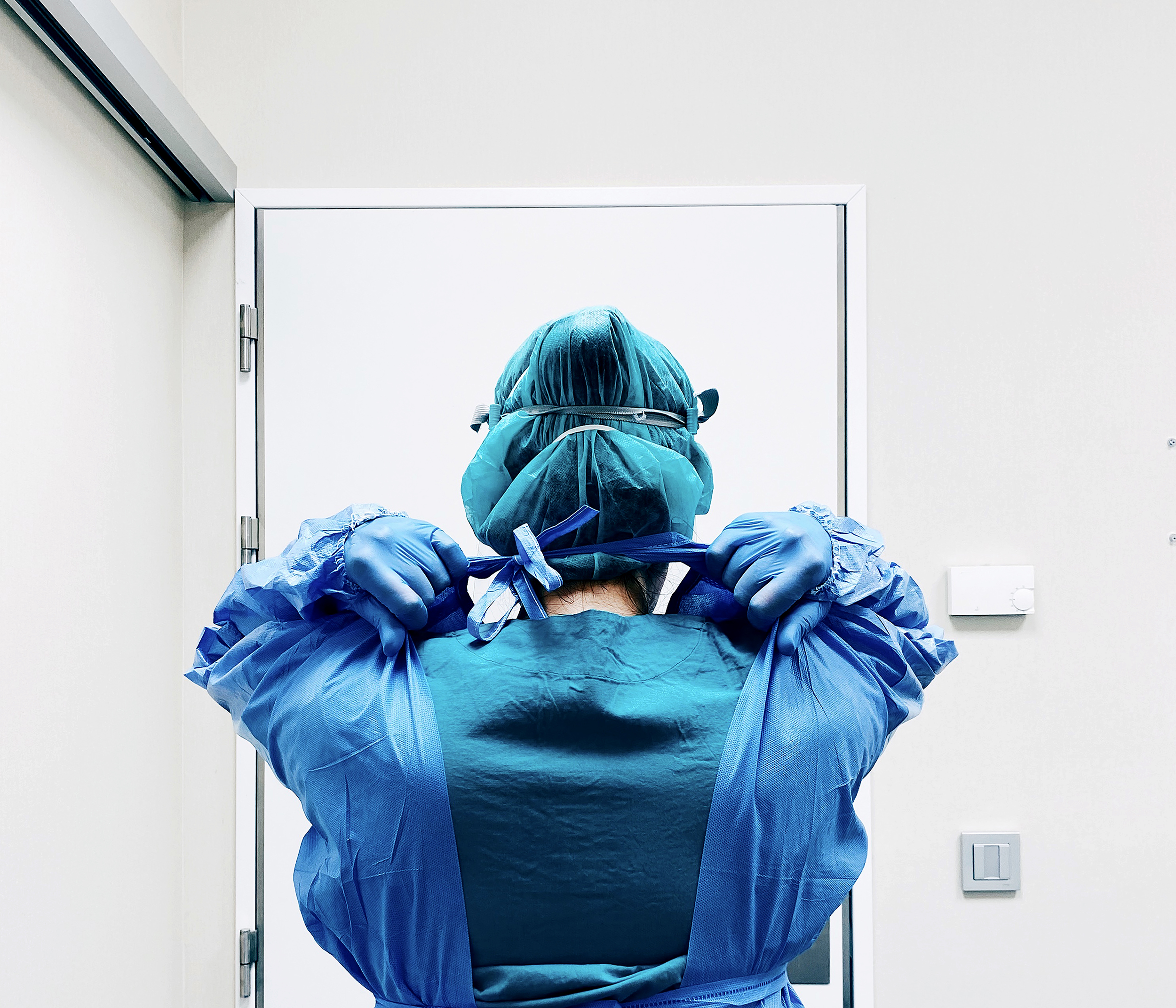 Enfermeira de costas retira equipamento de proteção individual azul.