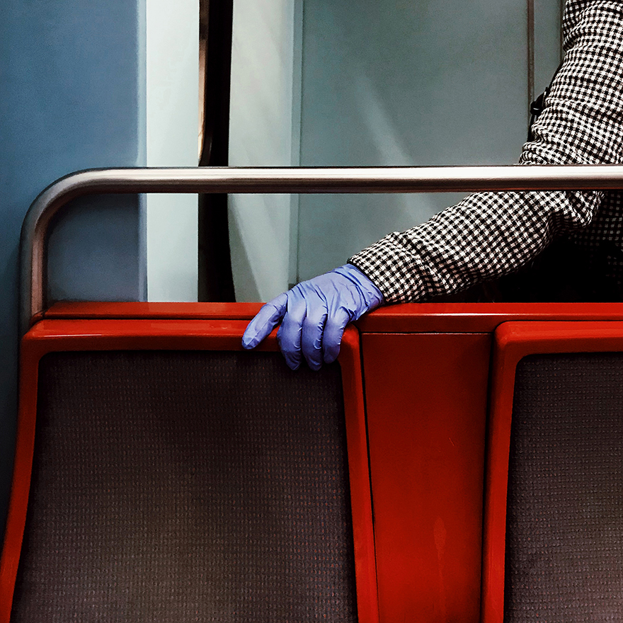 Mão com luva de látex roxa agarra costas de assento do metro.