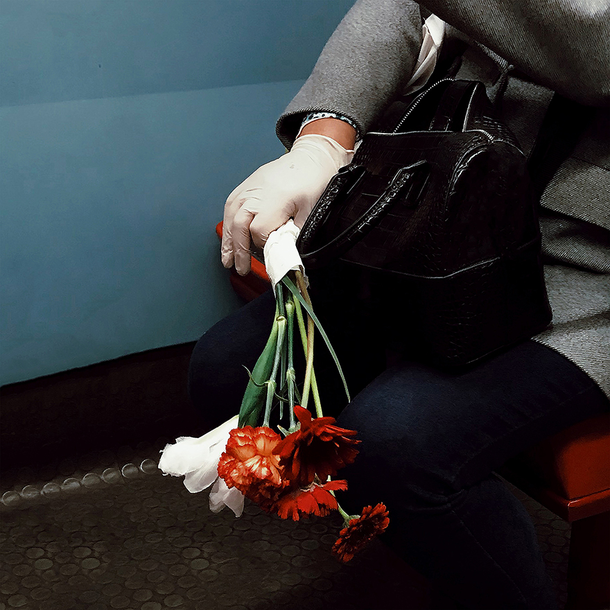 Mão com luva de látex branca agarra ramo de flores vermelhas.