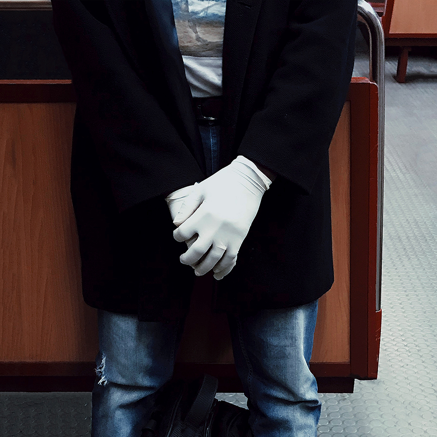 Mãos com luvas de látex brancas entrelaçadas, aliança nota-se no anelar da mão esquerda.