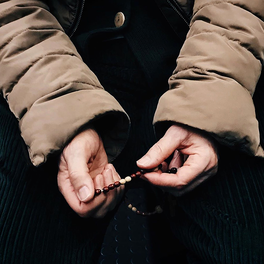 Mãos de mulher idosa mexem num terço.