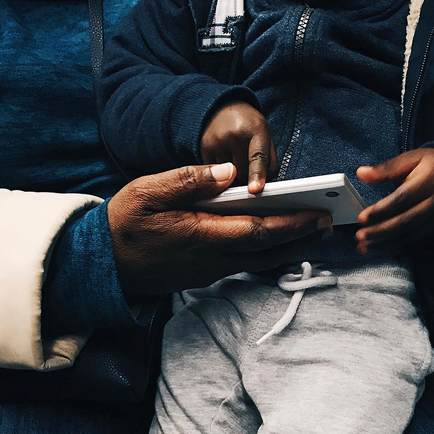 Mão de mulher adulta agarra telemóvel e mãos de criança tocam no telemóvel.