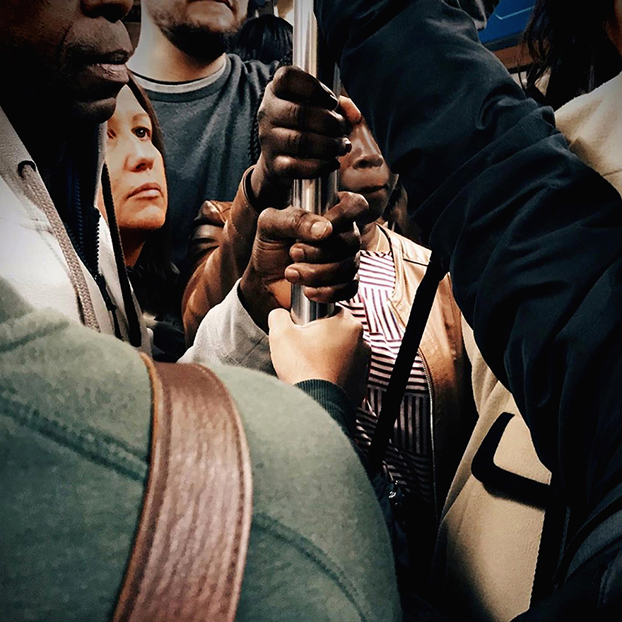 Mãos de várias pessoas próximas a agarrar a poste vertical do metro.