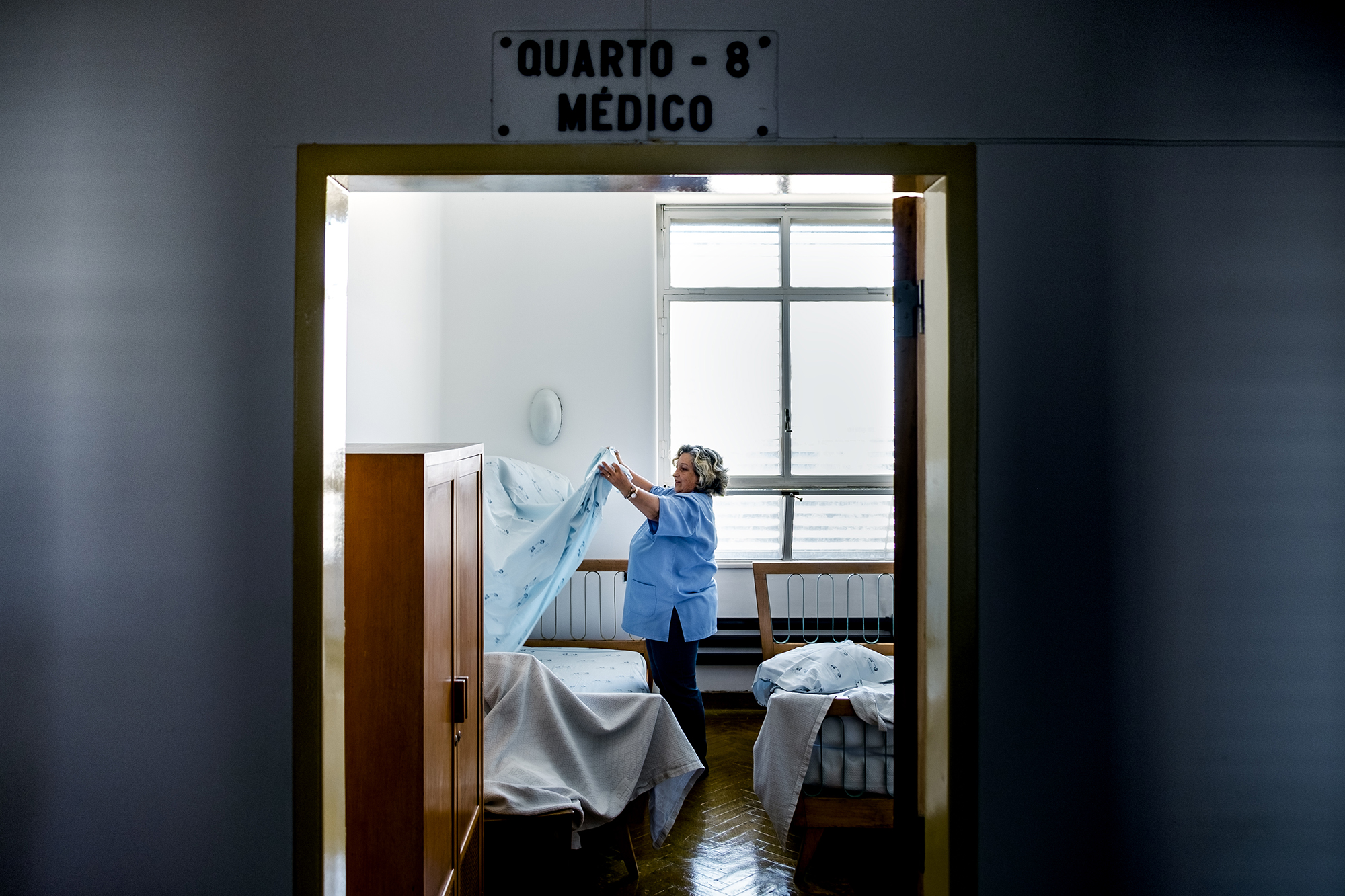 Mulher faz a cama no quarto médico, estendendo lençol.