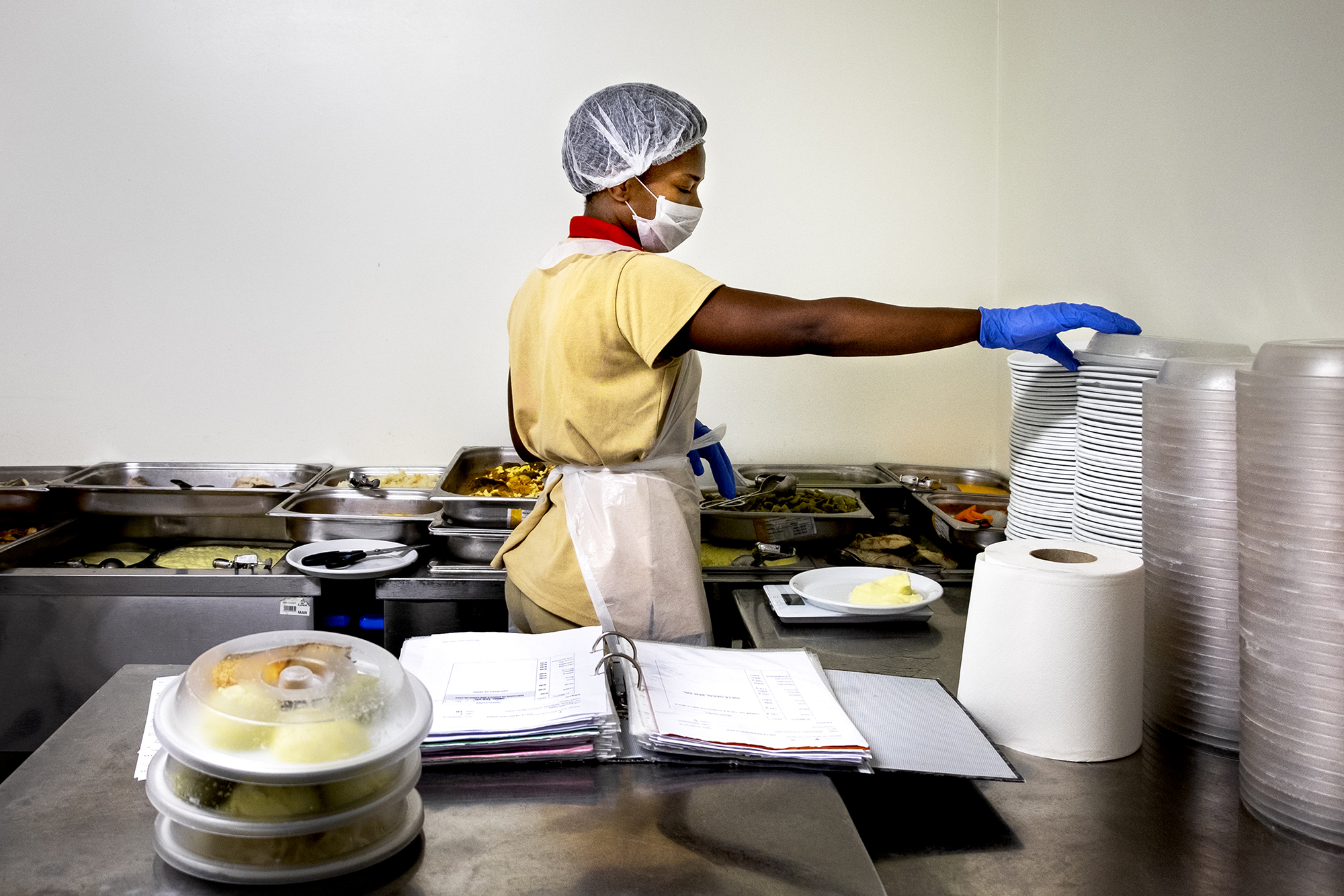 Mulher agarra um prato com o braço direito rodeada de tabuleiros com comida.